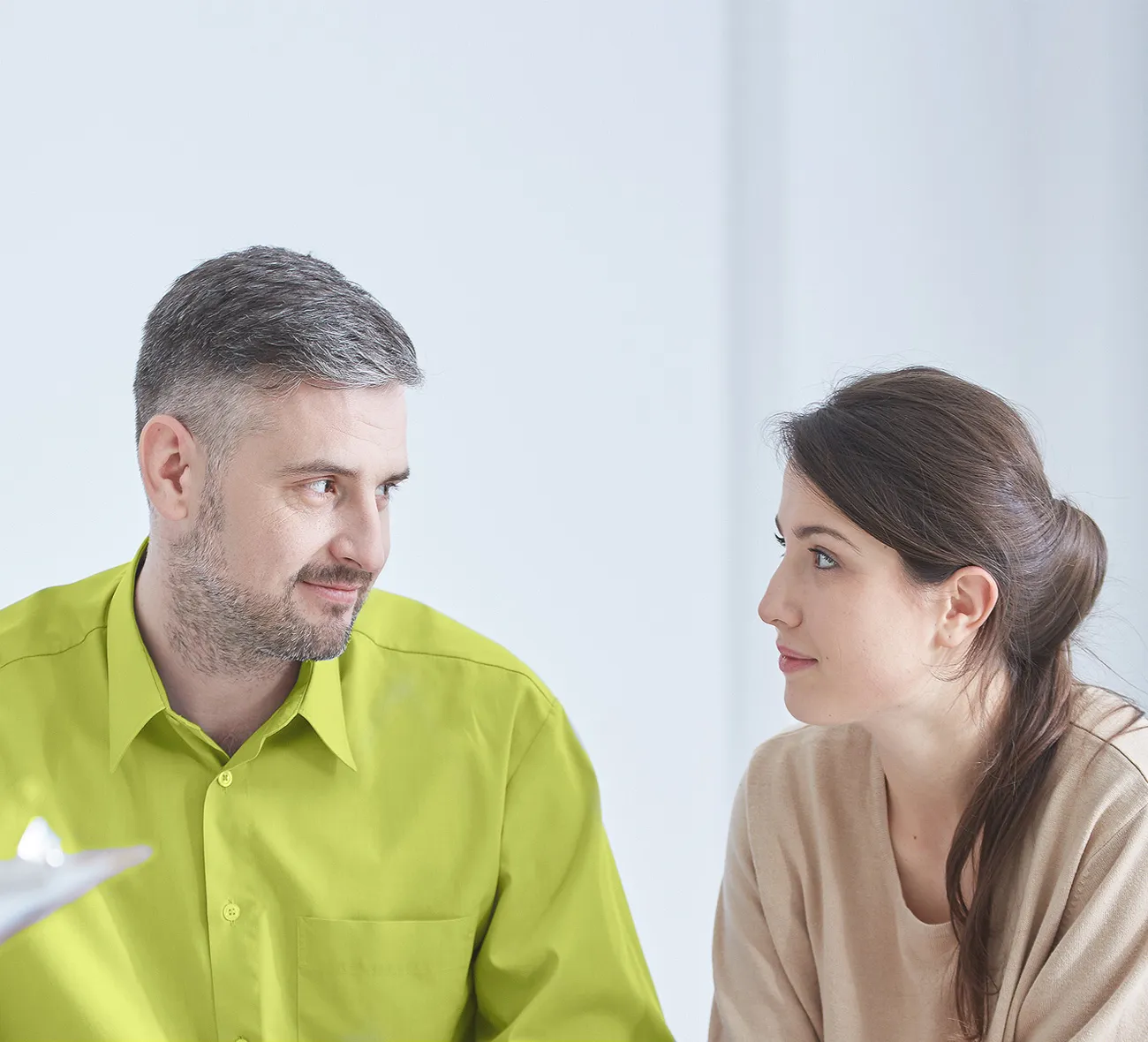 vorschau_paarcoaching Ein Paar sitzt bei einer Beratungssitzung, beide schauen sich an, während eine dritte Person mit einem Klemmbrett im Vordergrund steht.